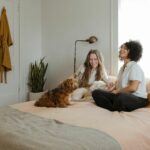 woman in white long sleeve shirt sitting on bed beside brown dog